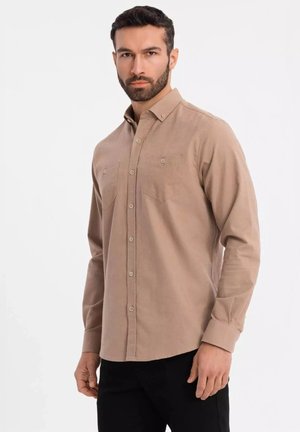 Chemise beige à manches longues avec col boutonné, deux poches poitrine et tissu texturé. Associée à un pantalon noir.