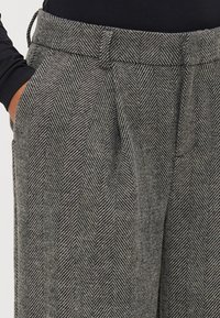 Pelēki bikses ar suniņu zobu rakstu, brīvā piegriezumā, ar sānu kabatām, jostu ar regulējamām saitēm un smalku tekstūru.