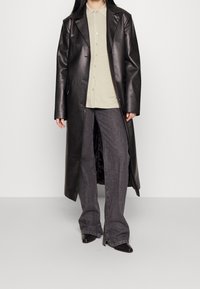 Svart läder lång kappa, ljusgrön skjorta med krage, grå utställda jeans. Slät textur, knappad skjorta, svarta skor med spetsig tå.