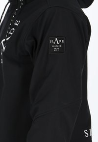 Felpa nera con cappuccio realizzata in tessuto morbido, con chiusura frontale a zip, cappuccio con coulisse e toppa sulla spalla con il marchio "SLADE COUTURE" in bianco.
