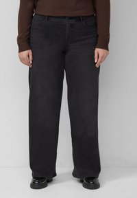 Czarne dżinsy o szerokich nogawkach wykonane z denimu o gładkiej fakturze, z przednimi kieszeniami i wysokim stanem. Noszone z czarnymi butami.