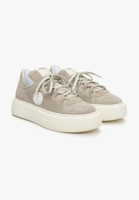 Szare zamszowe sneakersy z zaokrąglonymi białymi gumowymi podeszwami, z płaskimi sznurówkami i okrągłym detalem logo z boku.