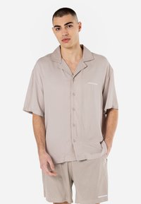 Lysbeige kortærmet skjorte med krave, fem knapper og broderet logo. Sæt med matchende strukturerede shorts.