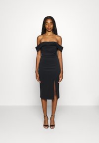 Robe noire sans épaule avec un corsage ajusté et une jupe à longueur genoux dotée d'une fente sur le côté. Tissu lisse, design minimaliste et sans motifs visibles.