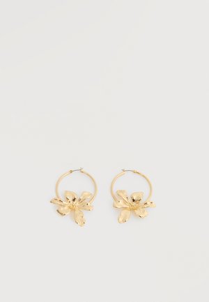 Boucles d'oreilles créoles en or avec de grandes breloques texturées en forme de fleur, présentées sur un fond blanc uni.