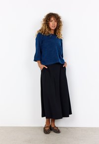 Blue textured sweater with three-quarter sleeves, paired with a black, pleated maxi skirt. Brown shoes with yellow accents complete the outfit.