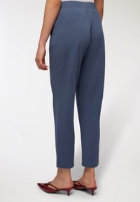 Niebieskie, zwężane spodnie z elastycznym paskiem, gładkiego materiału, z bocznymi kieszeniami, zestawione z czerwonymi klapkami na obcasie.