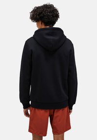 Sort hættebluse med blød tekstur, der har en kengurulomme og ribbede manchetter. Båret med orange shorts.