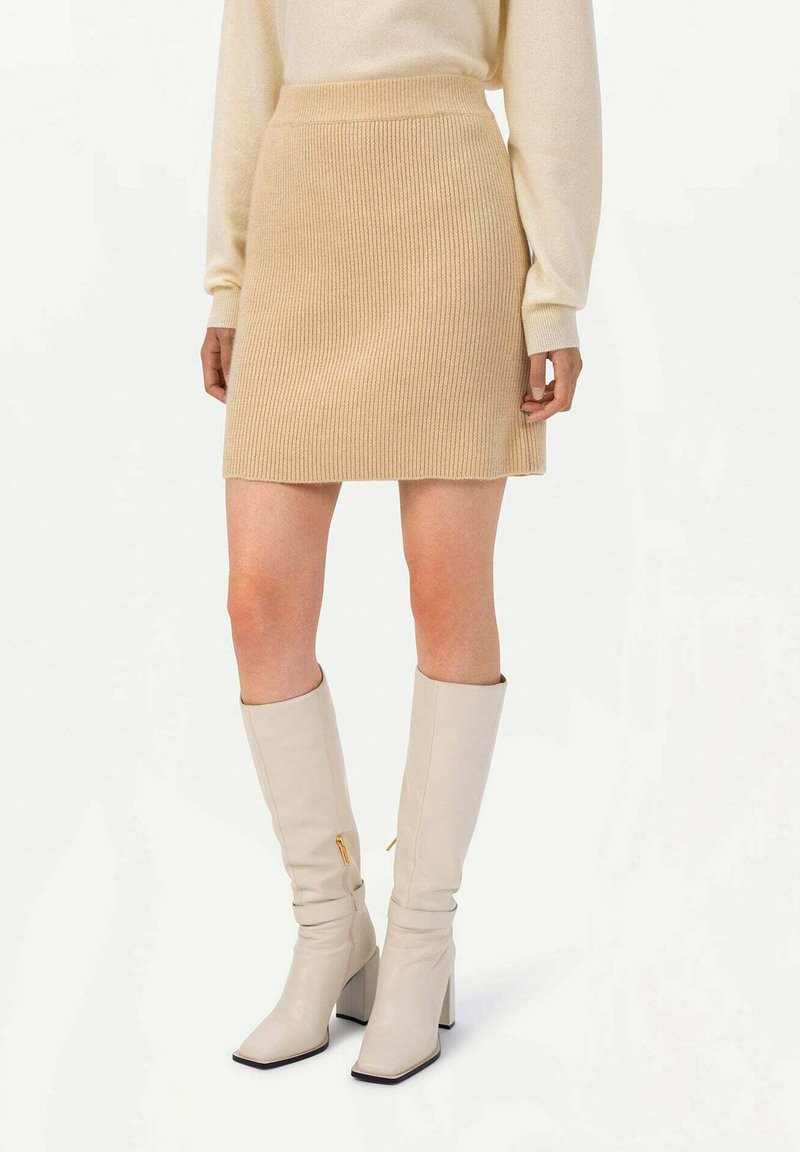 Beige stickad minikjol med ribbad struktur, i kombination med knähöga krämfärgade stövlar med klack och sidsidizipper.