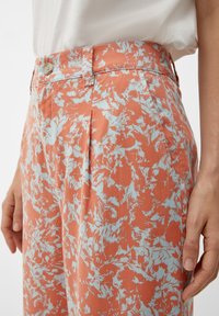 Pantaloni a fiori arancioni e blu con vita alta, dotati di chiusura anteriore con bottone e tasche laterali, realizzati in tessuto texturizzato.