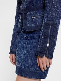 Giacca di jeans con una finitura testurizzata di blu scuro, dotata di tasche con cerniera e una silhouette aderente, abbinata a una gonna di jeans coordinata.