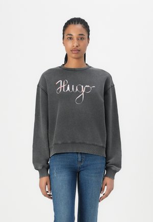 Felpa grigia con scollo rotondo, spalle drop e vestibilità ampia. Presenta un logo scritto "Hugo" in rosa sul davanti.