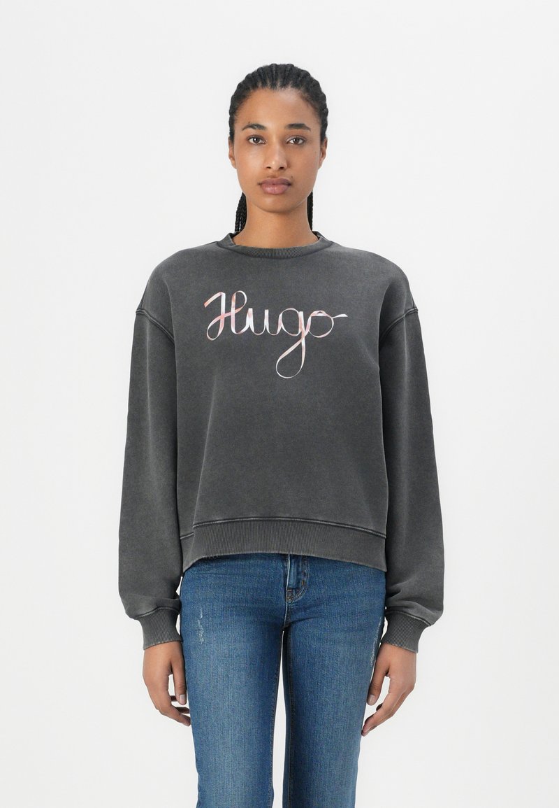 Gray sweatshirt with a round neckline, drop shoulders, and a loose fit. Features a script "Hugo" logo in pink on the front.