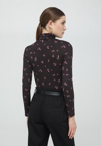 Top nero a maniche lunghe con un motivo floreale, caratterizzato da un colletto alto. Abbinato a pantaloni neri a vita alta e una cintura nera slender.