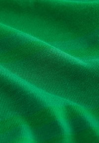 Zelená bavlnená látka s hladkou textúrou a diagonálnym vzorom tkania, zobrazujúca jemné záhyby a rôzne odtiene zelenej.