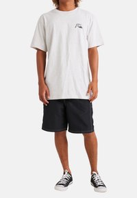 Camiseta de algodón gris claro con cuello redondo y mangas cortas, combinada con pantalones cortos negros con costuras blancas y zapatillas negras.