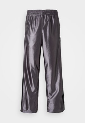Pantalons de sport gris brillants avec une coupe ample, une taille élastique et des accents noirs sur les côtés. La texture semble lisse et agréable.