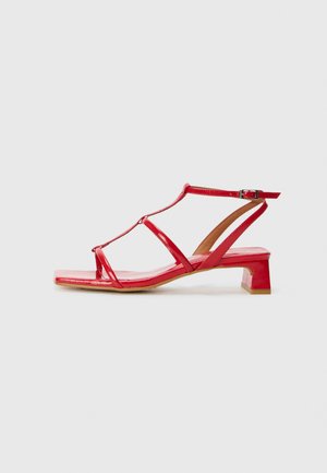 Red patent leather sandals with a T-strap design, square toe, small block heel, and adjustable ankle strap.