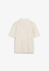 Kurzärmliges Polo in Creme, aus glattem Stoff gefertigt. Mit klassischem Kragen und lässigem Schnitt mit seitlichen Schlitzen am Saum.