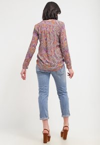 Halenka s dlouhým rukávem s paisley vzorem v purpurové, oranžové a modré barvě, volného střihu. Nosit s džínami v světle modré barvě a hnědými sandály na podpatku.