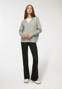 Maglione grigio chiaro oversize con scollatura a V, abbinato a pantaloni neri a righe sottili e sneakers bianche. Texture liscia, vestibilità casual.
