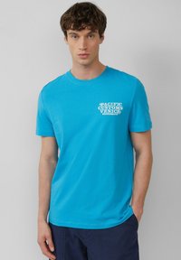 Turquoise katoenen t-shirt met korte mouwen, ronde halslijn en witte tekst met de tekst "PACIFIC CUSTOMS VENICE BOARDSKITS" op de borst.