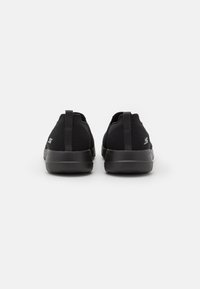 Baskets de sport noires avec une tige en maille, de forme arrondie et une semelle en caoutchouc texturé. Présentent un onglet de traction au niveau du talon et un logo discret sur le côté.