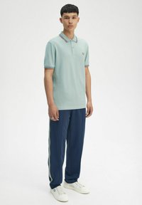 Ljusa blått polo-shirt med krage och kontrasterande randig trim, tillsammans med marinblåa träningsbyxor med sidosträck och vita sneakers.