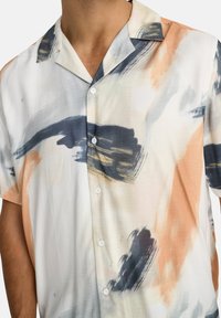 Camisa de manga corta en una tela ligera, con una mezcla de patrones de pinceladas abstractas en azul, naranja y crema. Cinco botones adornan el frente.