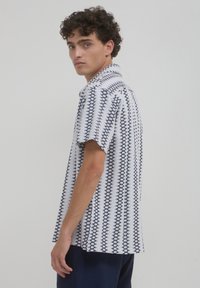 Chemise à manches courtes, colée, en blanc et bleu marine avec un motif géométrique. Tissu léger avec une coupe décontractée, dotée d'un ourlet droit.