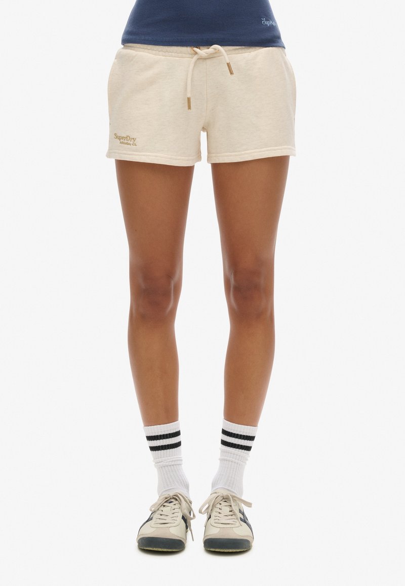 Shorts en coton beige avec un waistband à cordon de serrage et des accents dorés, présentant un petit logo brodé en bas à gauche.