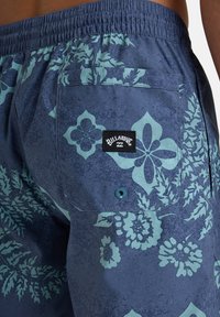 Billabong-uima shortsit tummansinisinä teal kukkakuosisina. Ominaisuudet: kuminauhavyötärö, sivutasku ja merkkilogo takana.