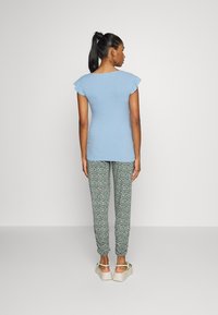 Top azul-claro com textura em ribas e mangas curtas com babados, combinado com calças verdes com padrão floral e sandálias chunky de cor clara.