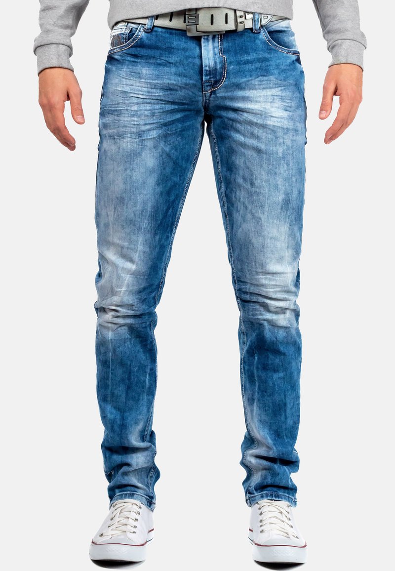 Jean en denim bleu clair avec un design délavé et usé. Dispose de cinq poches, de coutures contrastantes et d'une ceinture avec une boucle grise.