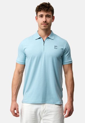Lyseblå poloshirt med korte ærmer. Har en krave og et lille sort logo på brystet. Stoffet ser glat og let tekstureret ud.