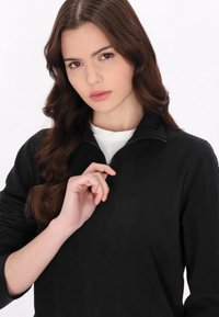 Sudadera de forro polar negra con cuello alto y una cremallera parcial. Presenta mangas largas, una textura suave y una silueta ajustada.