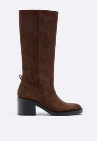 Brauner Wildleder-Stiefel bis zum Knie mit quadratischer Spitze, klobigem Absatz und Schlaufe hinten. Nahtdetails entlang der Seiten.