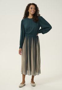 Pleated dress with a teal top and beige striped skirt. Long sleeves, elastic waist, and lightweight fabric for a flowing look.
