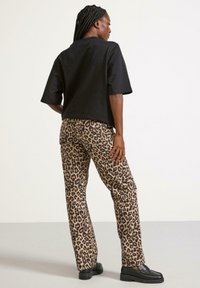 T-shirt noir oversize associé à un pantalon en imprimé léopard beige et marron, avec des jambes droites et des chaussures noires plates.
