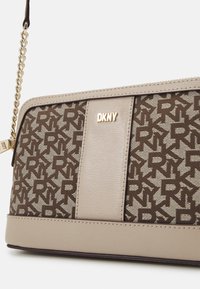 Sac à main DKNY marron en tissu texturé avec motif logo, accents beige lisses, quincaillerie dorée et fermeture à glissière.
