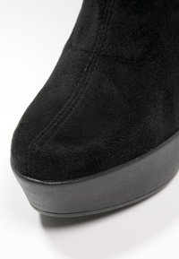 Chaussure plateforme en daim noir avec bout arrondi et coutures apparentes sur la partie supérieure.