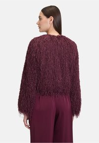 Pull court en velours bordeaux avec des manches longues, présentant un design à franges texturé. Assorti avec un pantalon coordonné, mettant en avant un tissu lisse.