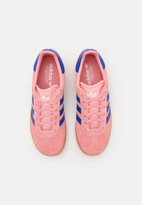 Pink suede sneakers with blue stripes, round toe, and gum rubber sole. Features laces and branding on the tongue.