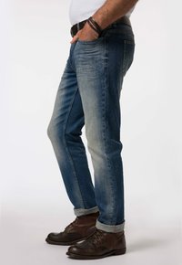 Blå denimjeans med en bleknad finish, rak bendesign och uppvikta fållar, tillsammans med bruna läderstövlar.