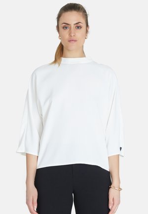 Top bianco con collo alto e maniche a tre quarti, realizzato in tessuto morbido; presenta una vestibilità ampia e un sottile logo decorativo.