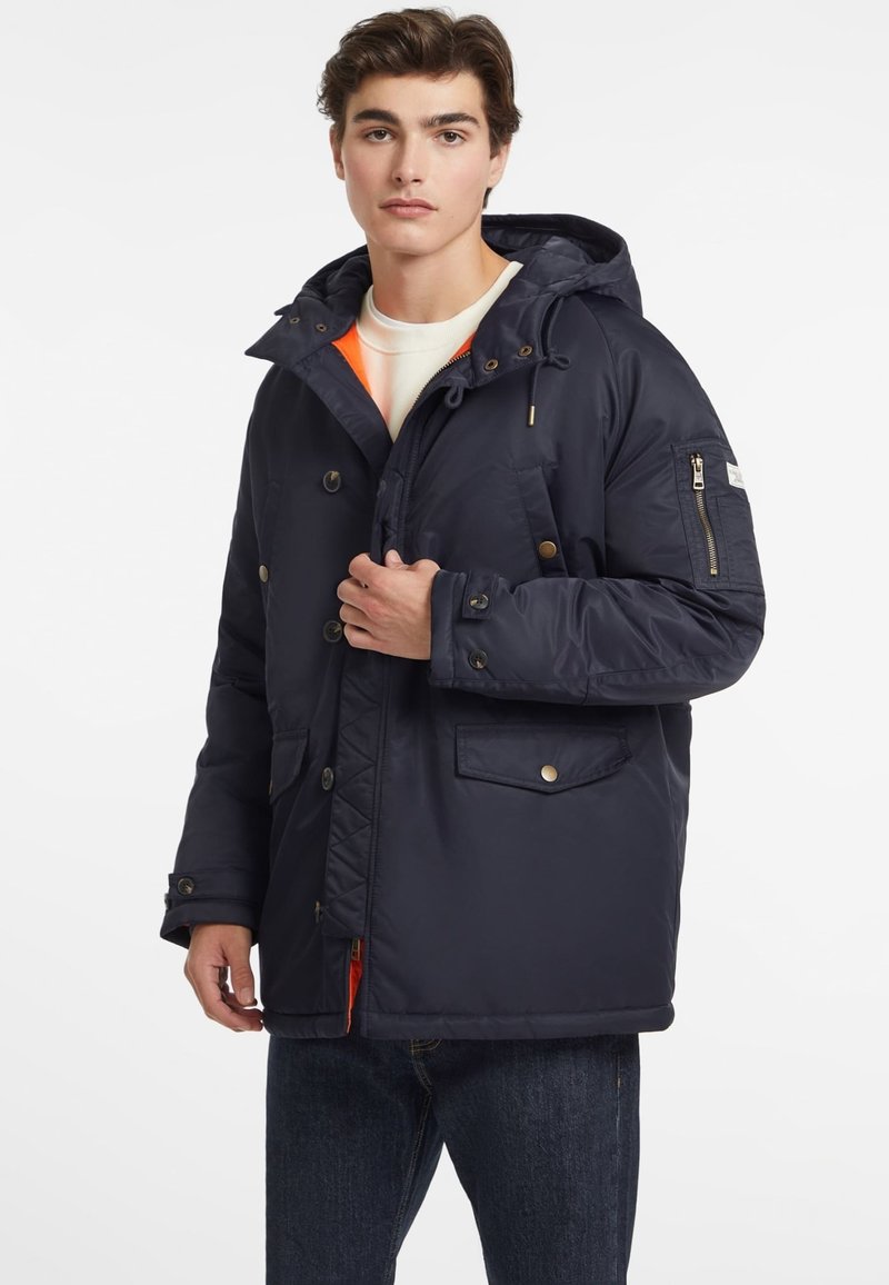 Chaqueta aislante de color azul marino con capucha, con botones dorados, múltiples bolsillos y un forro interior naranja para contraste.