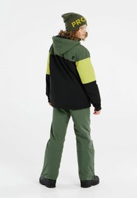 Veste de ski verte et noire avec capuche, dotée d'un design à blocs de couleurs. Associée à un pantalon vert et un bonnet vert avec écritures jaunes.