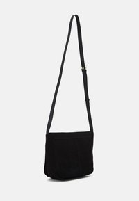 Černá semišová crossbody taška s plochým tvarem, nastavitelným popruhem a jednoduchým klopovým zavíráním. Má jemné švy a měkkou texturu.