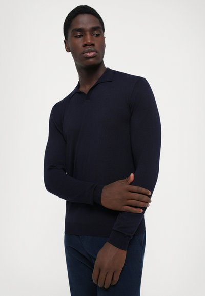 Navy blue long-sleeve polo shirt made of knitted fabric, featuring a classic collar and ribbed cuffs, worn with dark denim pants.