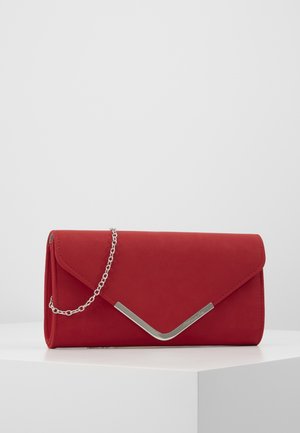 Czerwona kopertówka z metalowym detalem w kształcie litery V w kolorze srebrnym oraz łańcuszkiem na ramię, prezentowana na białym piedestale na jednolitym tle.